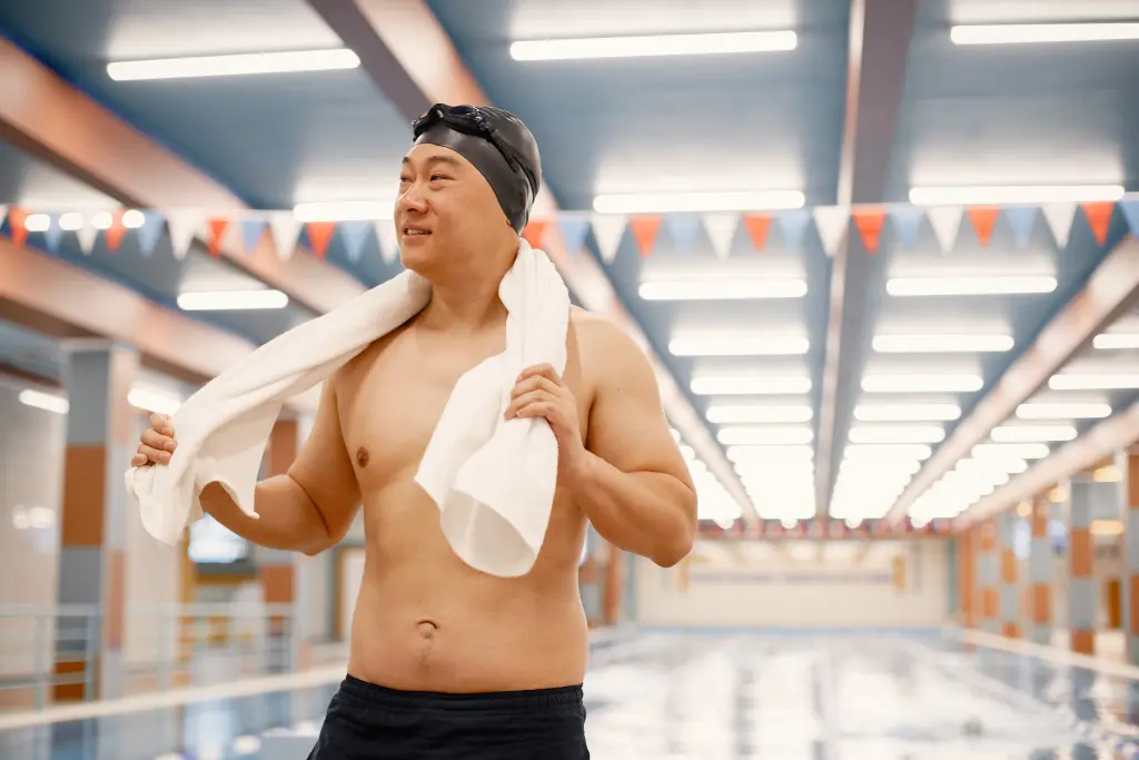 asian-man-standing-in-indoors-swimming-pool-with-a-towel-on-his-shoulders.jpg